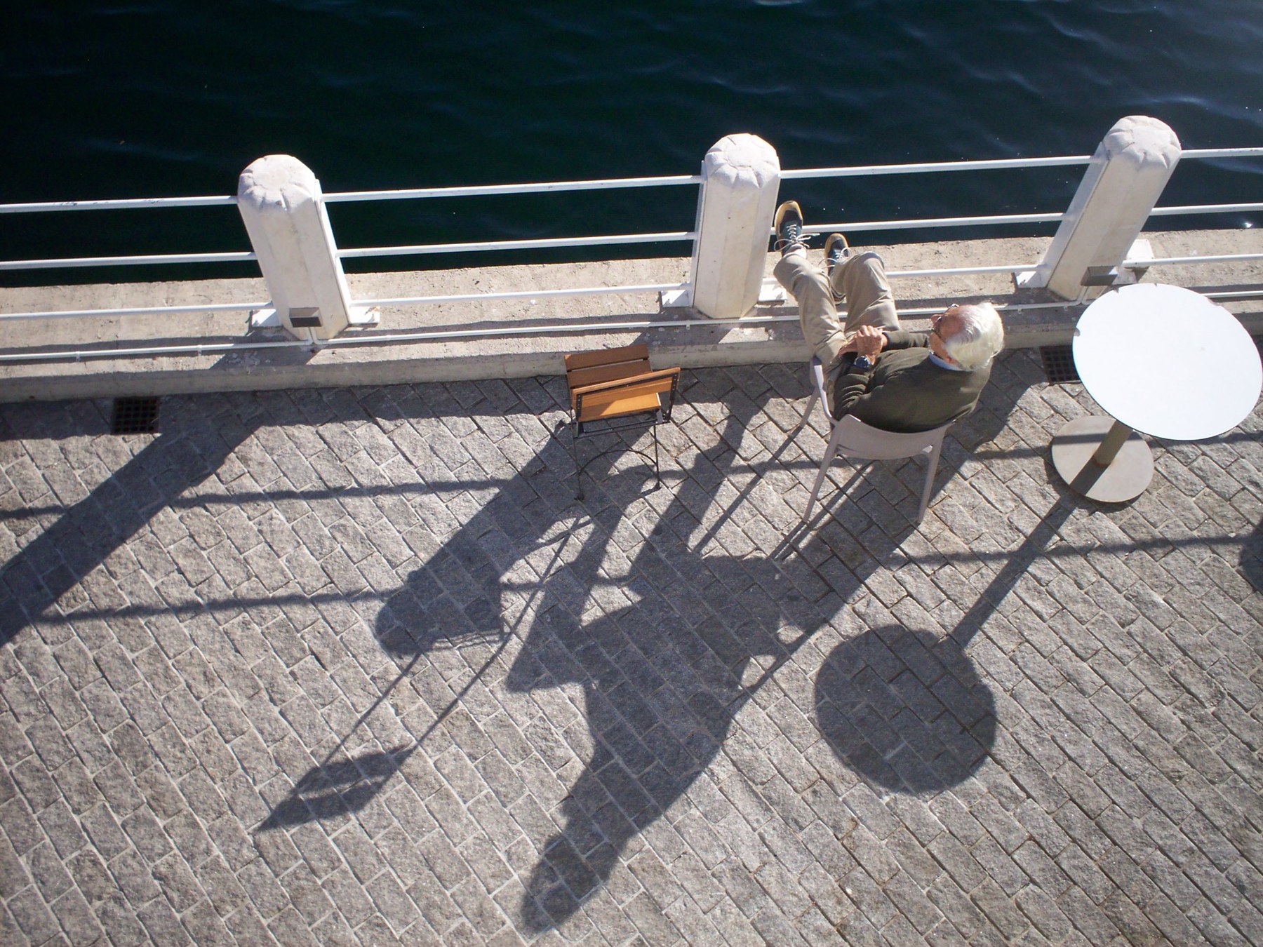 An overhead view of a seated man and diagonal shadows beside the water.