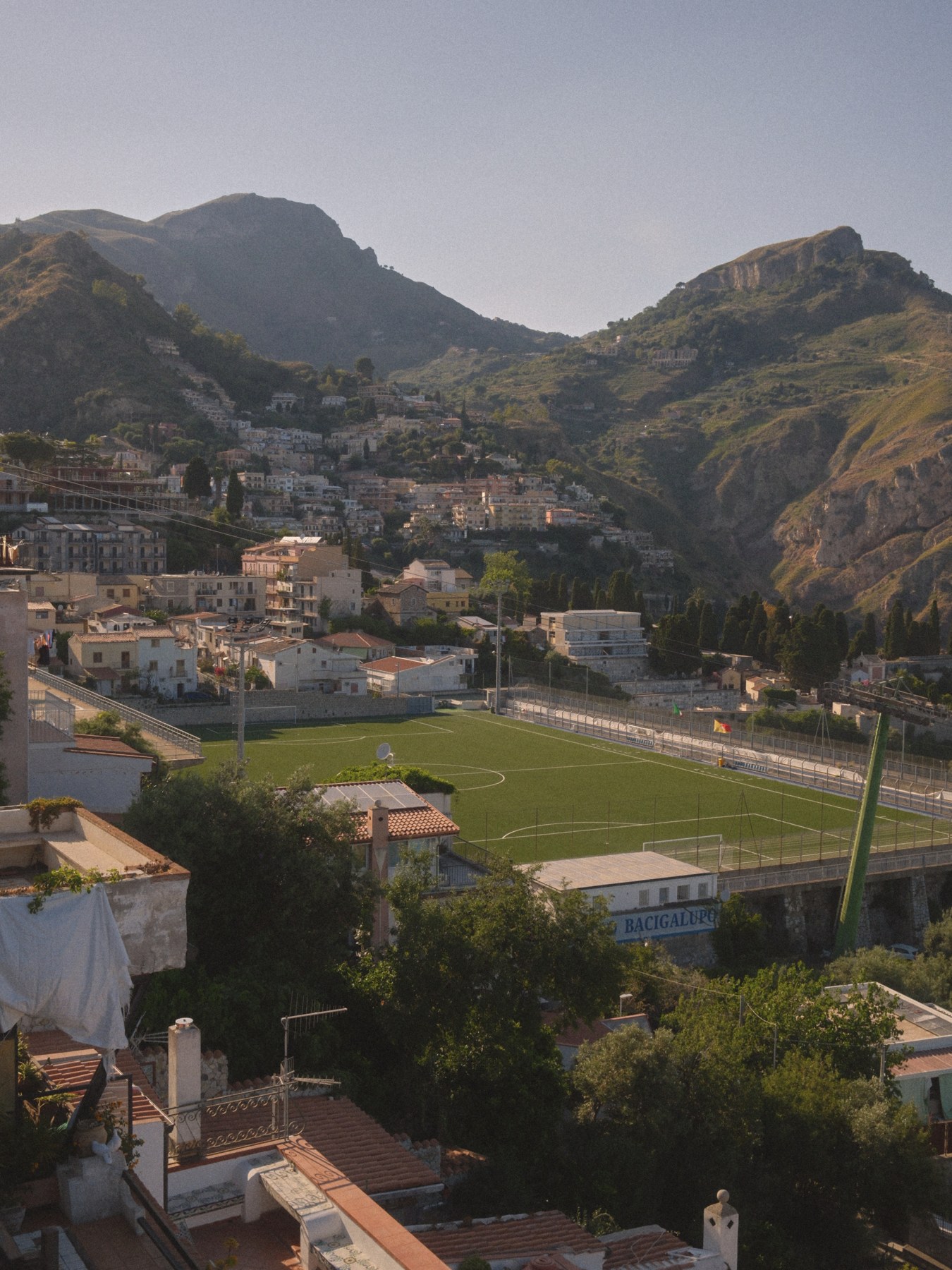 A football pitch in a valley surrounded by mountains and buildings.