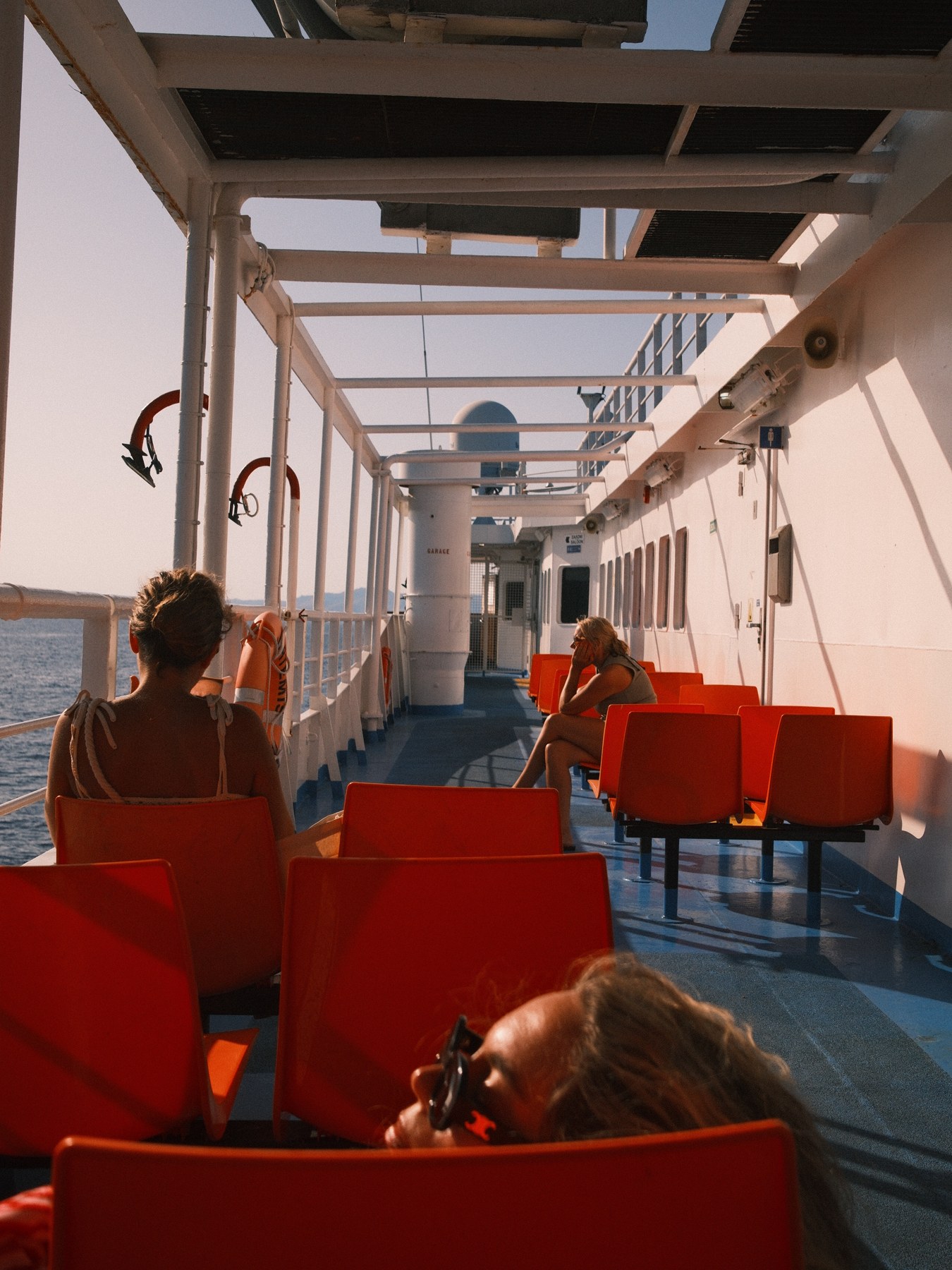 Red seats and passengers inside a sunlit ferry.